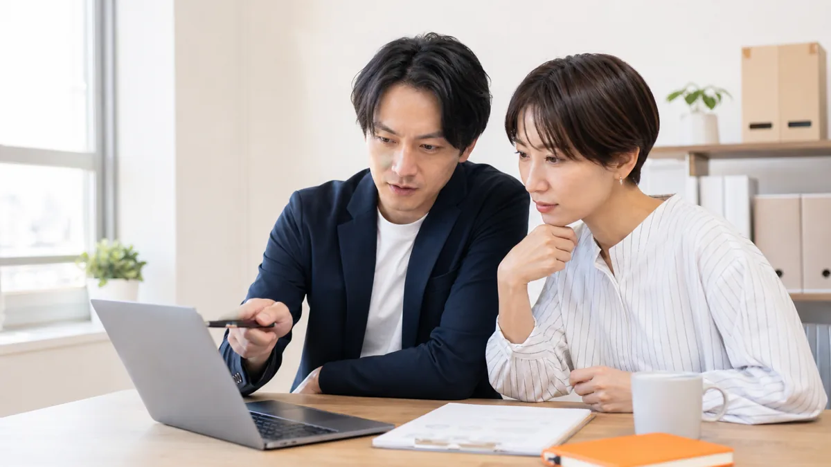 オフィスでノートパソコンの文章を2人のスタッフが並んで確認している様子