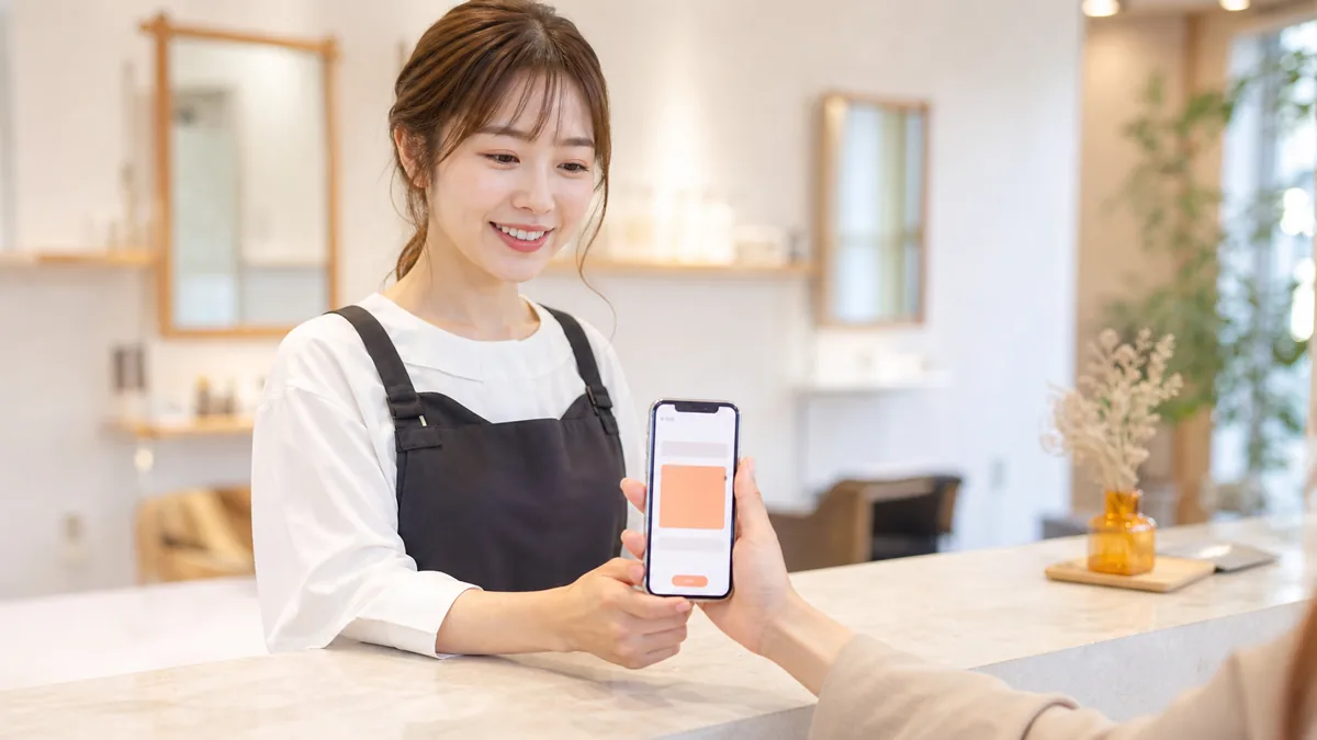 レジカウンターで顧客のLINEクーポン画面を確認する美容室スタッフの写真