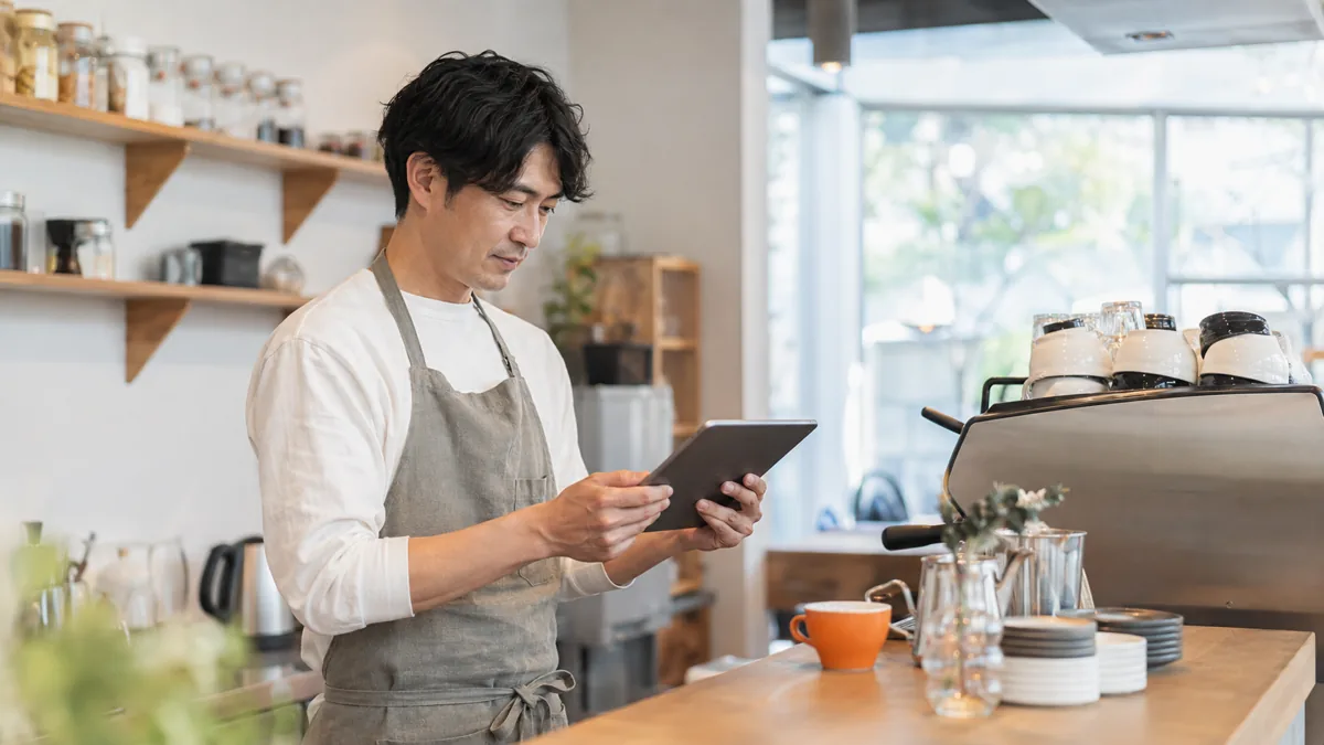 カフェのカウンターでタブレットのGoogleビジネスプロフィール画面を見ながら口コミを確認するオーナー