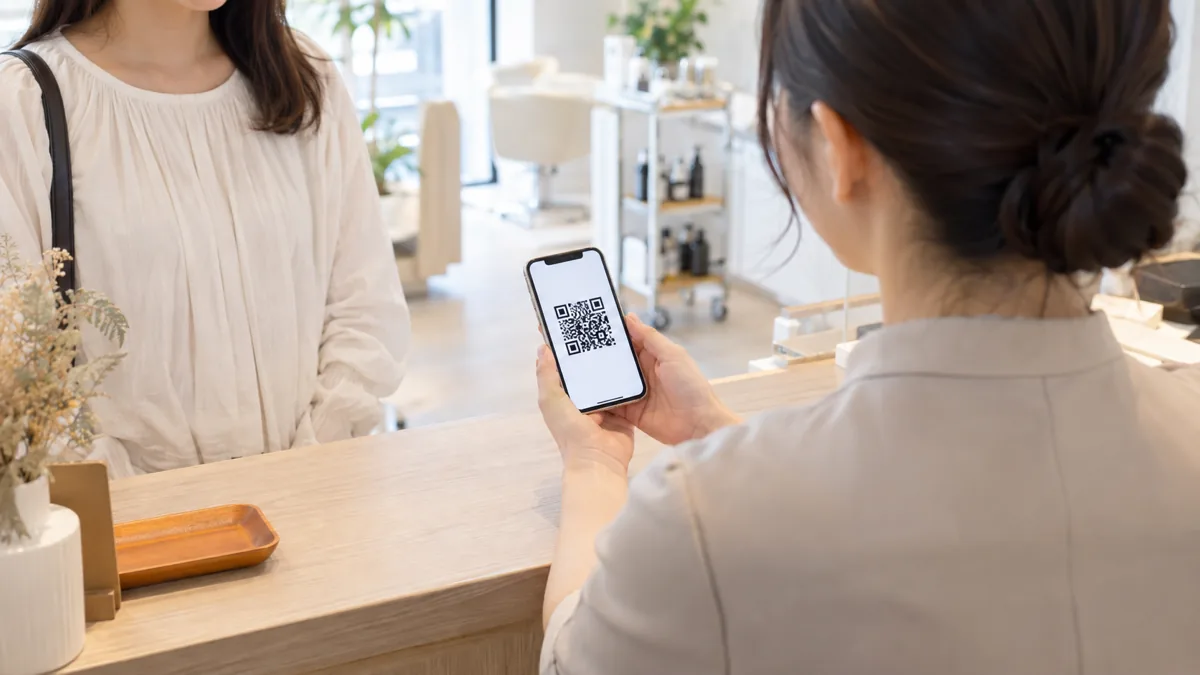 美容サロンの受付でスタッフが来店客にLINE公式アカウントの友だち追加画面を見せている後ろ姿の写真